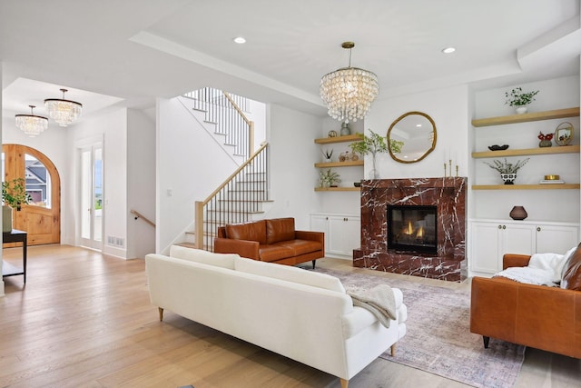 living room with a notable chandelier, built in features, a tray ceiling, light hardwood / wood-style floors, and a fireplace