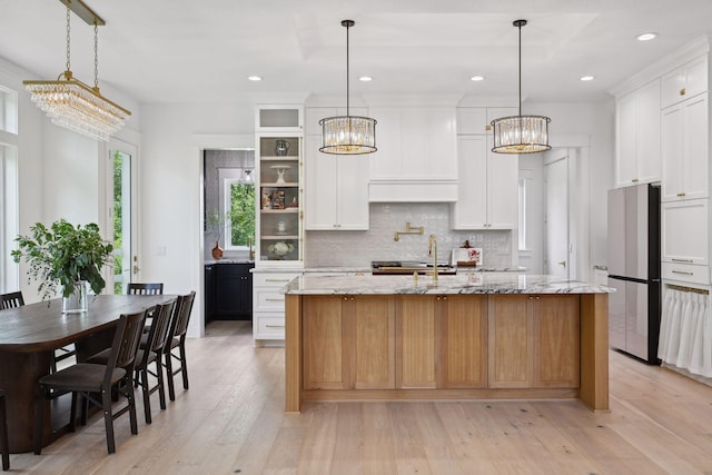 kitchen featuring white cabinetry, light wood-type flooring, stainless steel fridge, and light stone countertops