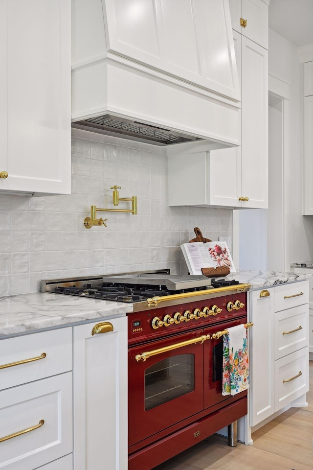 kitchen featuring white cabinetry, custom range hood, light wood-type flooring, backsplash, and range with two ovens