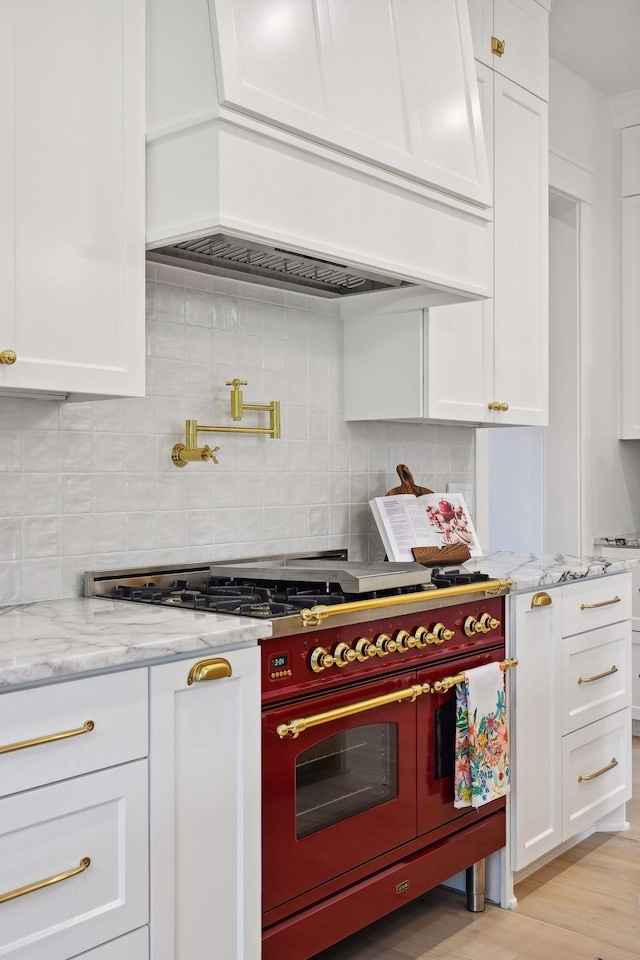 21412 Poate Ct, Rogers, MN 55374 - kitchen featuring double oven range, white cabinetry, light wood-style floors, decorative backsplash, and custom range hood
