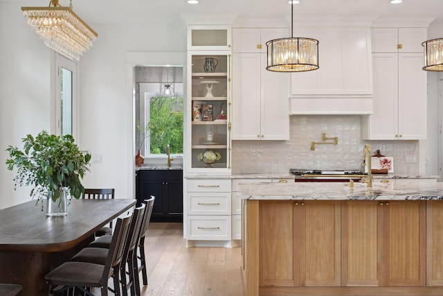 kitchen with decorative backsplash, white cabinetry, decorative light fixtures, and light wood-type flooring