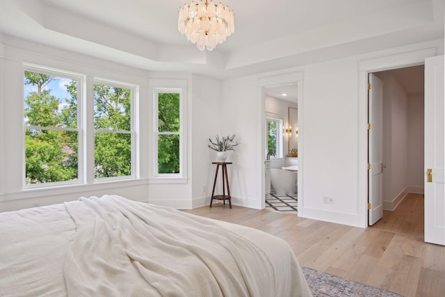 bedroom featuring a tray ceiling, light hardwood / wood-style flooring, connected bathroom, and a notable chandelier