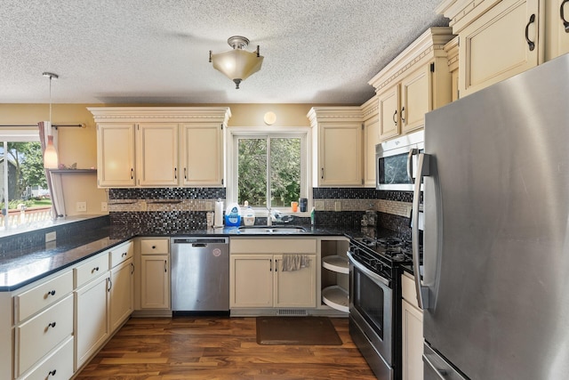 kitchen featuring appliances with stainless steel finishes, decorative light fixtures, sink, dark hardwood / wood-style flooring, and cream cabinets