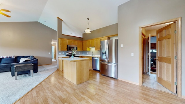 kitchen with decorative light fixtures, a center island, light wood-type flooring, and stainless steel appliances