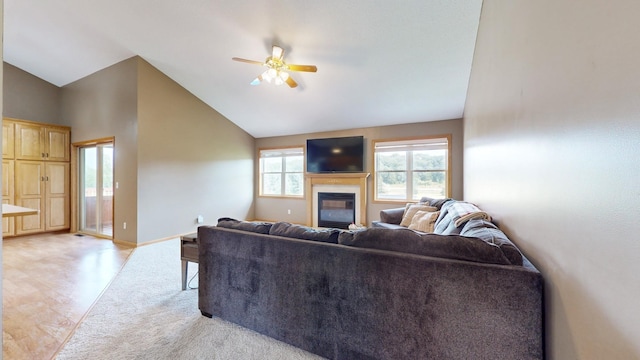 living area featuring lofted ceiling, a glass covered fireplace, ceiling fan, and baseboards