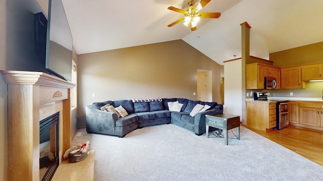 living area with lofted ceiling, ceiling fan, a glass covered fireplace, and light colored carpet