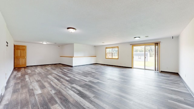 empty room with a textured ceiling, wood finished floors, and baseboards