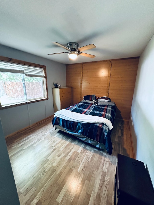 bedroom featuring wood walls, ceiling fan, and light wood-type flooring