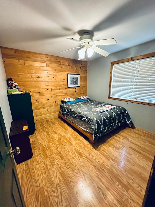 bedroom featuring ceiling fan, light hardwood / wood-style floors, and wood walls