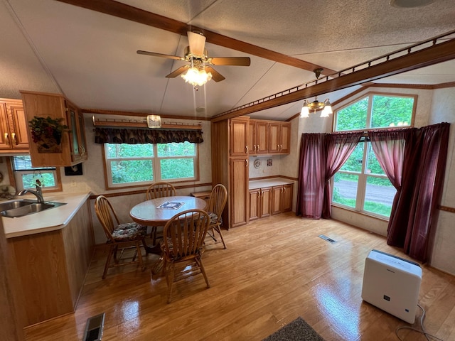 dining area featuring light wood-type flooring, a textured ceiling, sink, vaulted ceiling with beams, and ceiling fan