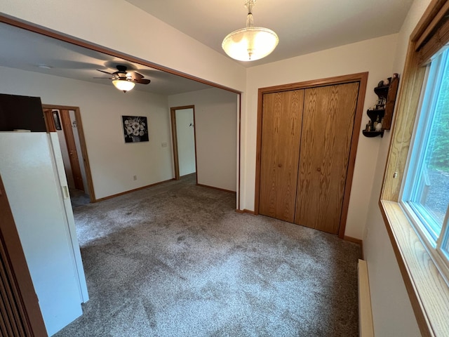 unfurnished bedroom featuring white fridge, carpet flooring, a baseboard heating unit, and a closet