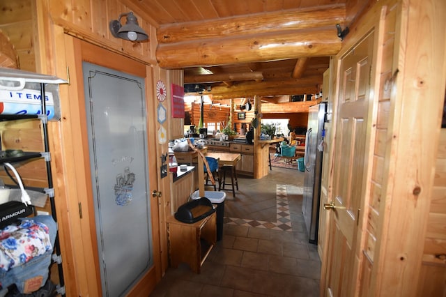 kitchen featuring beam ceiling, stainless steel refrigerator, tile patterned floors, and rustic walls