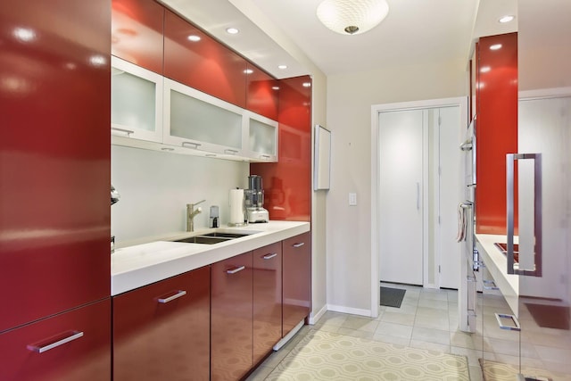 kitchen featuring a sink, recessed lighting, light countertops, light tile patterned floors, and red cabinets