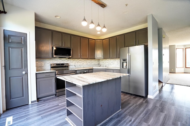 kitchen with appliances with stainless steel finishes, backsplash, decorative light fixtures, a center island, and dark wood-type flooring