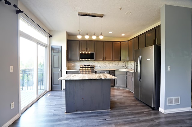 kitchen featuring dark hardwood / wood-style flooring, a kitchen island, appliances with stainless steel finishes, decorative light fixtures, and sink