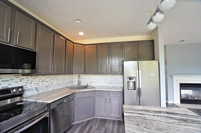 kitchen featuring a multi sided fireplace, stainless steel appliances, sink, pendant lighting, and dark wood-type flooring