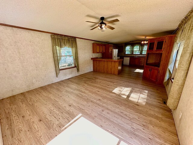 unfurnished living room with hardwood / wood-style flooring, ceiling fan with notable chandelier, ornamental molding, vaulted ceiling, and a textured ceiling