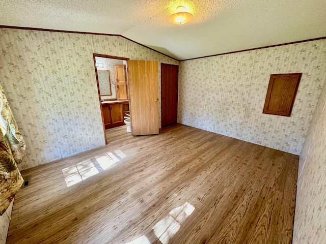 unfurnished bedroom with ensuite bathroom, light hardwood / wood-style floors, crown molding, a textured ceiling, and lofted ceiling