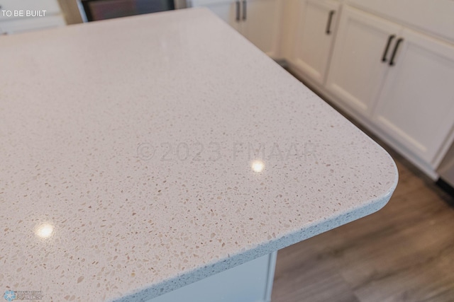 interior details featuring white cabinetry, light stone counters, and dark wood-type flooring