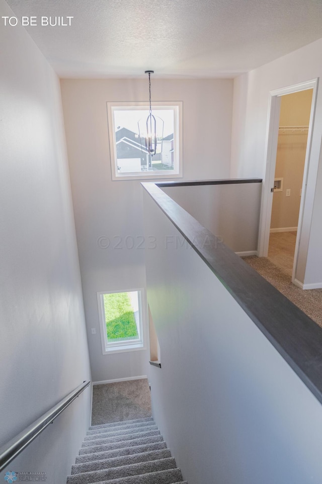 staircase with carpet flooring, an inviting chandelier, and a textured ceiling