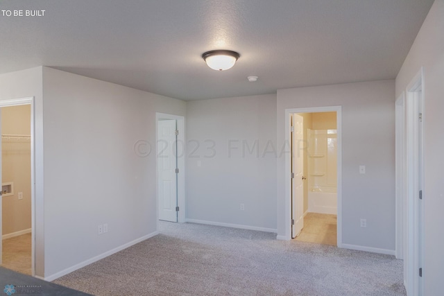 unfurnished bedroom with light carpet, connected bathroom, and a walk in closet