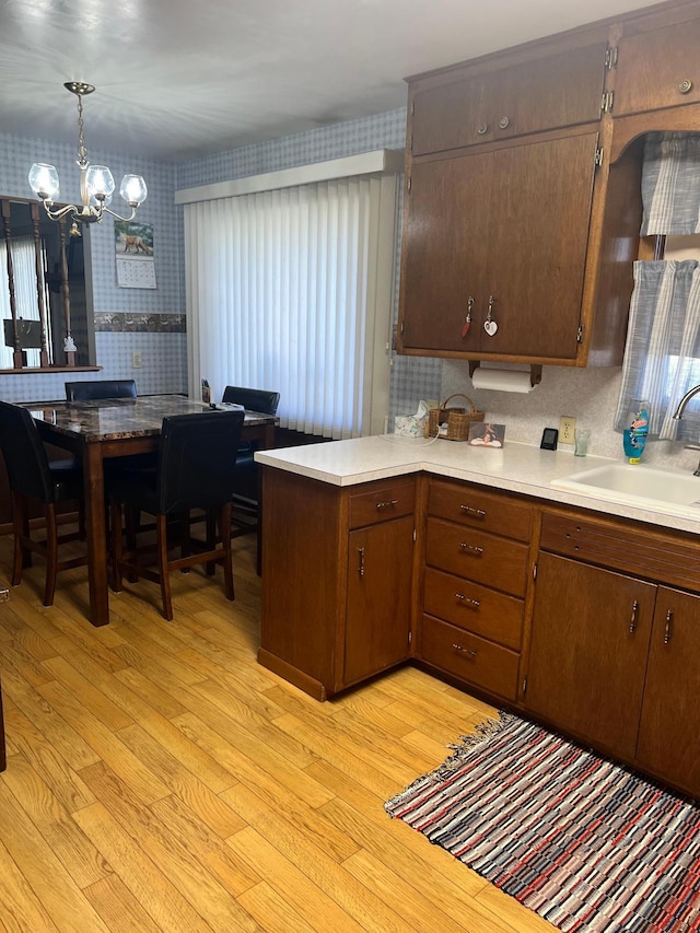 618 Memorial Pl, Dawson, MN 56232 - kitchen featuring wallpapered walls, light wood-style flooring, a sink, a chandelier, and a peninsula