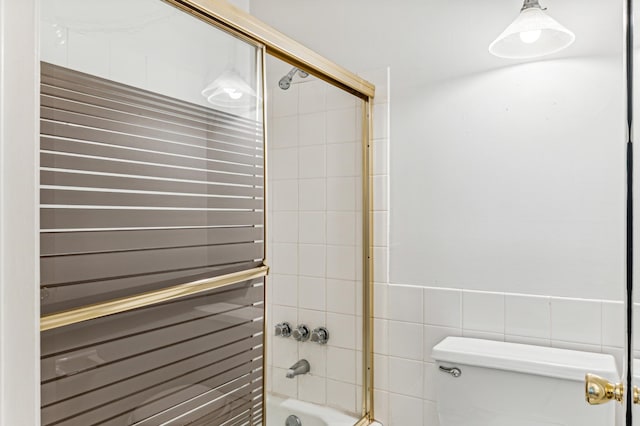 bathroom with toilet, shower / bath combination with glass door, and tile walls