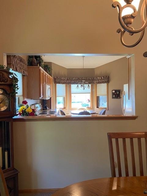 kitchen with a notable chandelier, stove, a peninsula, white microwave, and hanging light fixtures