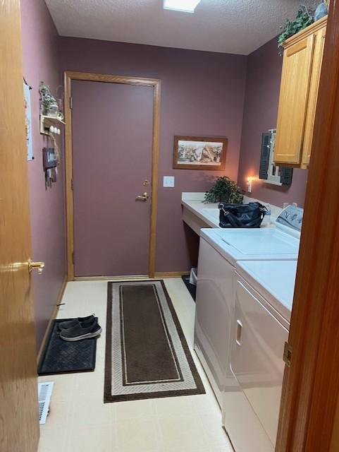 clothes washing area with washer and dryer, cabinet space, and a textured ceiling