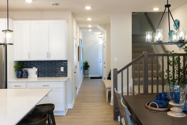 kitchen featuring white cabinetry, hanging light fixtures, tasteful backsplash, and light wood-type flooring