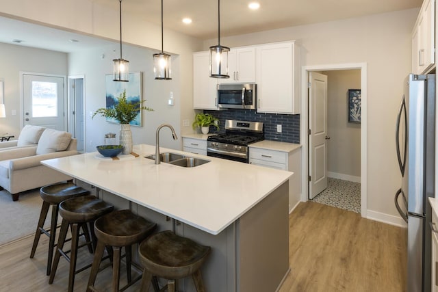 kitchen with white cabinetry, sink, a kitchen bar, stainless steel appliances, and a center island with sink