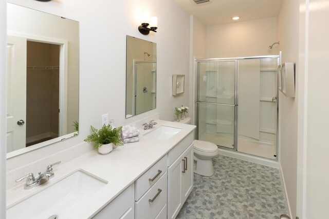 bathroom featuring a shower with shower door, tile patterned flooring, toilet, and dual bowl vanity