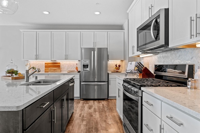 kitchen with white cabinetry, light hardwood / wood-style floors, appliances with stainless steel finishes, light stone counters, and sink