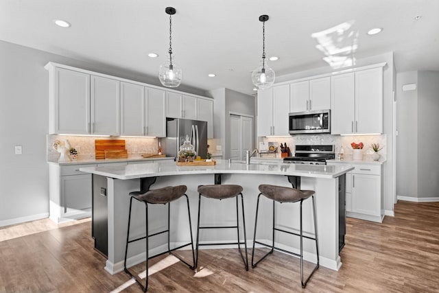 kitchen featuring white cabinets, a kitchen island with sink, stainless steel appliances, and pendant lighting