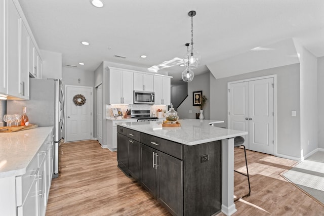 kitchen with hanging light fixtures, white cabinets, stainless steel appliances, and a center island