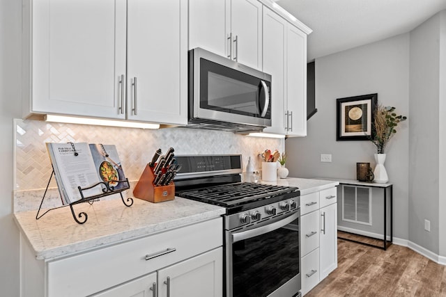 kitchen with light hardwood / wood-style floors, decorative backsplash, white cabinetry, stainless steel appliances, and light stone counters