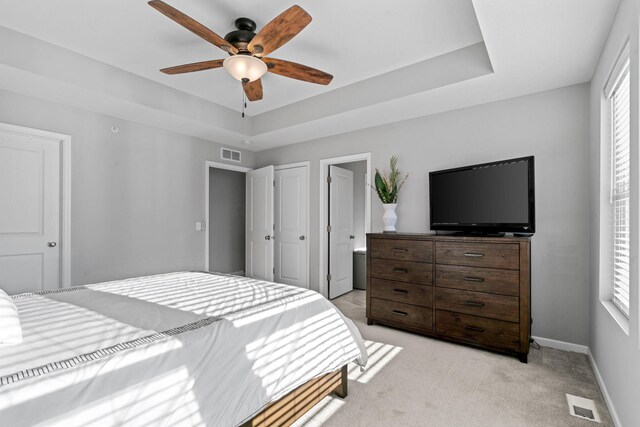 carpeted bedroom with ceiling fan and a tray ceiling