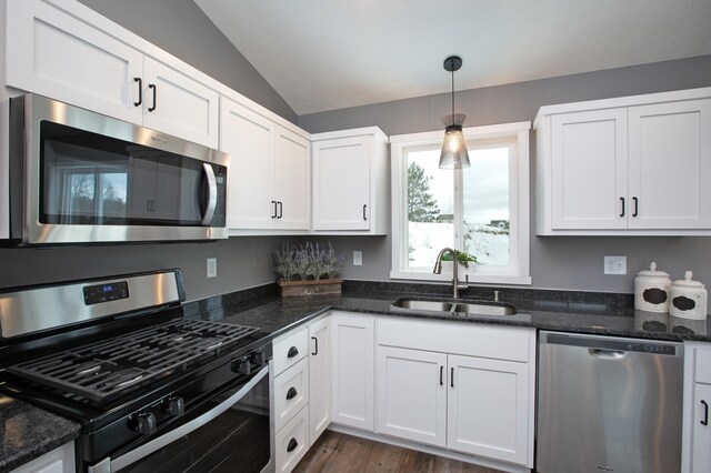 kitchen with appliances with stainless steel finishes, vaulted ceiling, sink, decorative light fixtures, and dark wood-type flooring