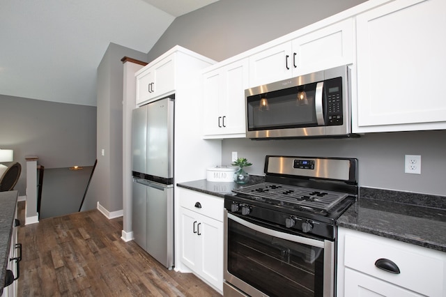 kitchen featuring lofted ceiling, appliances with stainless steel finishes, white cabinetry, dark hardwood / wood-style floors, and dark stone counters