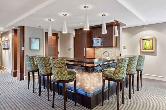 bar with stainless steel microwave, dark brown cabinets, carpet, decorative light fixtures, and tasteful backsplash