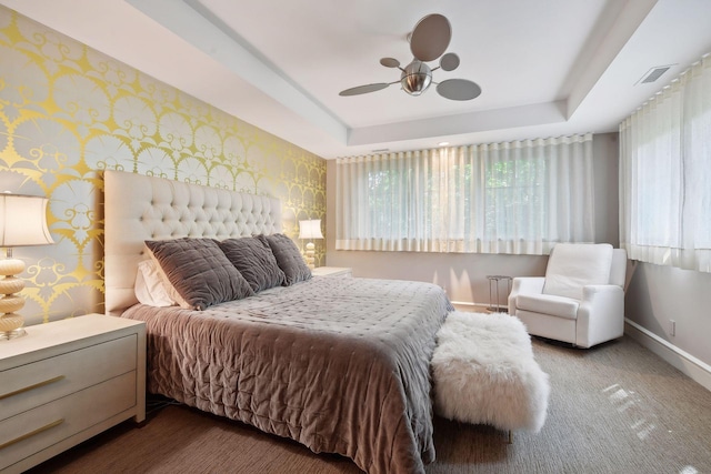 carpeted bedroom with ceiling fan, a tray ceiling, and multiple windows