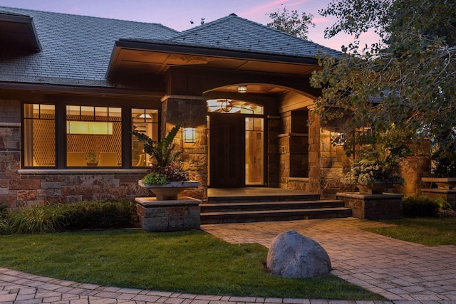 entrance to property with stone siding, a high end roof, and a lawn