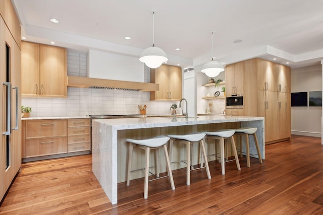 kitchen featuring open shelves, a sink, light brown cabinets, wall chimney exhaust hood, and a kitchen bar
