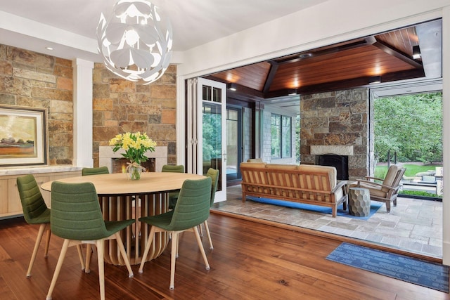 dining area with a stone fireplace, a chandelier, and wood-type flooring