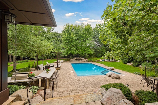 swimming pool with a patio area, a diving board, a yard, and view of scattered trees