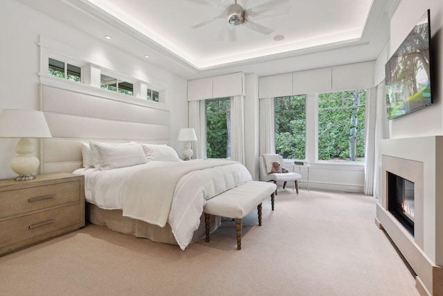 bedroom with multiple windows, light colored carpet, a glass covered fireplace, and a raised ceiling