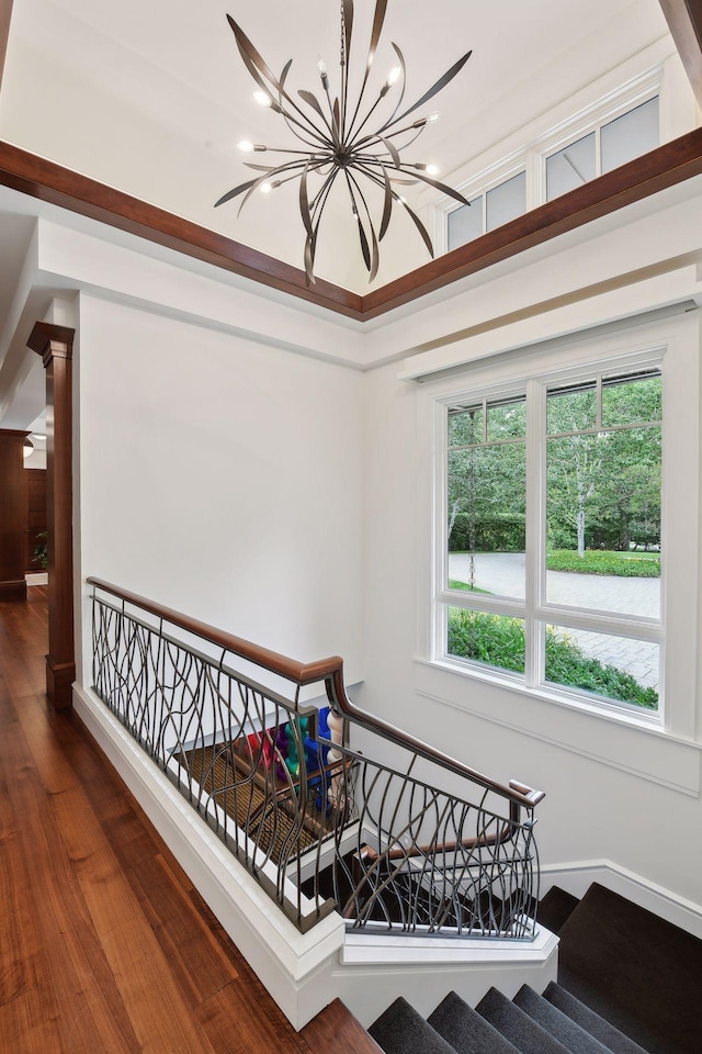 stairway with healthy amount of natural light, a chandelier, wood finished floors, and ornate columns