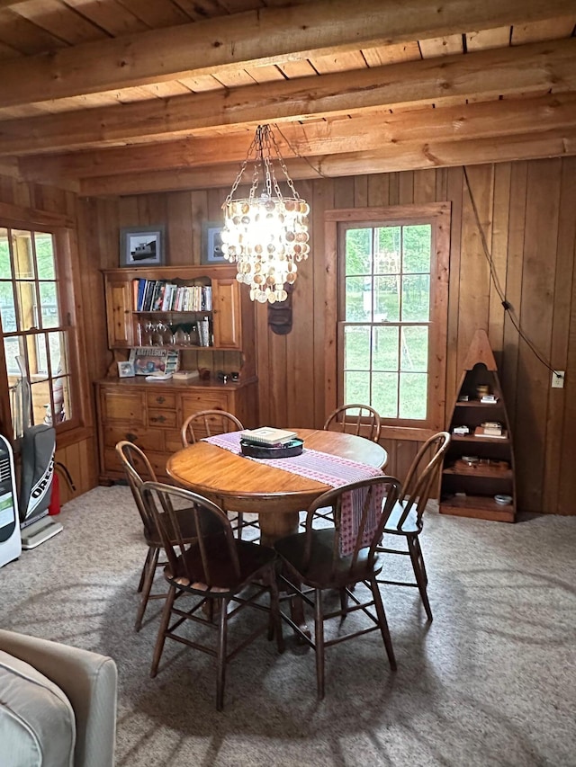 dining area with an inviting chandelier, wood walls, carpet, and beam ceiling