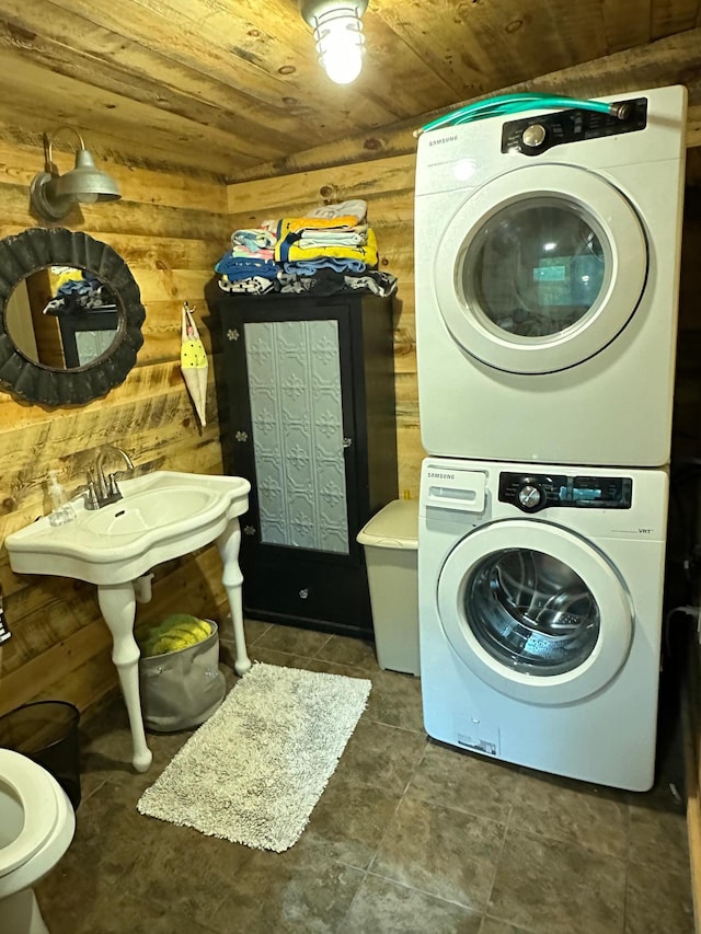 clothes washing area featuring stacked washer and dryer, dark tile patterned floors, wood walls, and wooden ceiling