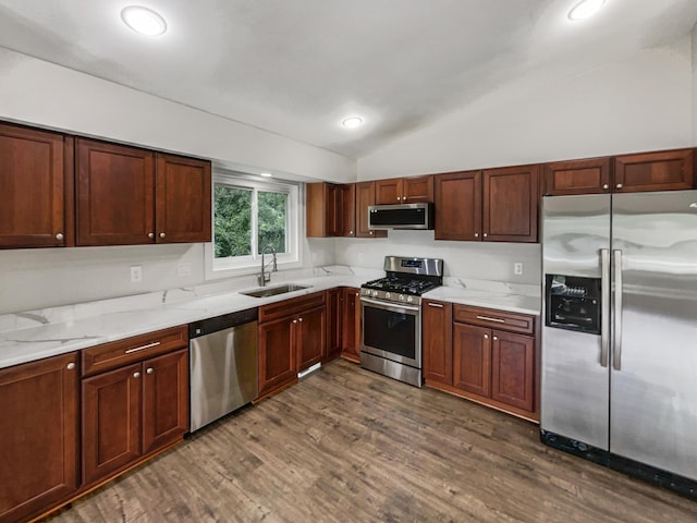 kitchen featuring appliances with stainless steel finishes, dark wood-type flooring, light stone counters, lofted ceiling, and sink